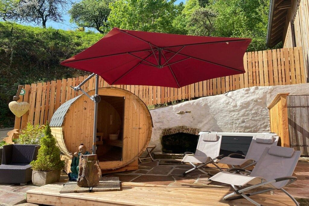 Una terraza de madera con sauna, asientos al aire libre y un paraguas rojo.