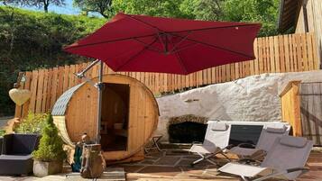 Una terraza de madera con sauna, asientos al aire libre y un paraguas rojo.