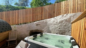 A hot tub with a wooden deck and a stone wall in a backyard setting.