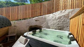 Un jacuzzi con cubierta de madera y pared de piedra en un jardín.