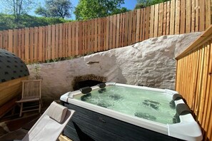 Ein Whirlpool mit Holzterrasse und Steinmauer in einem Garten.