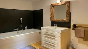 A bathroom with a bathtub, a white vanity with drawers, a mirror with a wooden frame, and a towel rack.