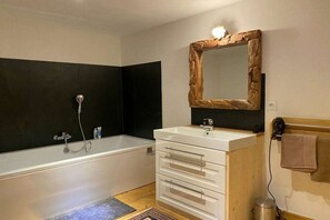 Ein Badezimmer mit einer Badewanne, einem weißen Waschtisch mit Schubladen, einem Spiegel mit Holzrahmen und einem Handtuchhalter.