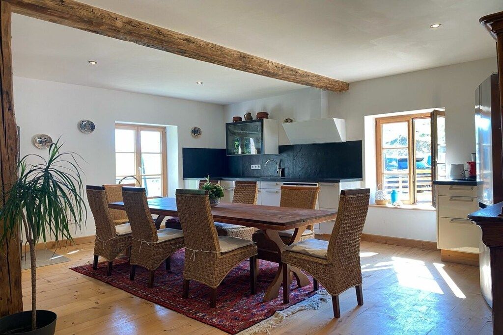 Un comedor con una mesa de madera y sillas de mimbre, una planta en maceta y vistas a la cocina.