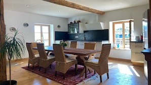 A dining area with a wooden table and wicker chairs, a potted plant, and a view of the kitchen.