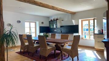 Un comedor con una mesa de madera y sillas de mimbre, una planta en maceta y vistas a la cocina.