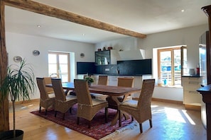 Ein Essbereich mit einem Holztisch, Korbstühlen, einer Zimmerpflanze und Blick auf die Küche.
