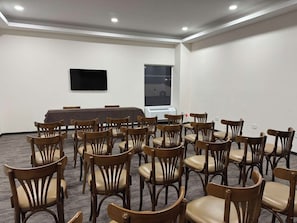 A conference room with a long table and chairs, a flat-screen TV, and a window with a view of a vehicle.