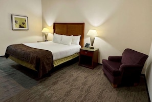 A hotel room with a bed, two bedside lamps, a nightstand, a chair, and a framed picture on the wall.