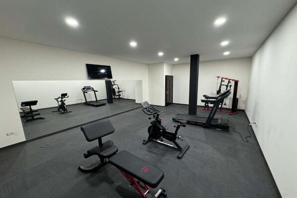 A gym with exercise equipment, benches, and a television on the wall.