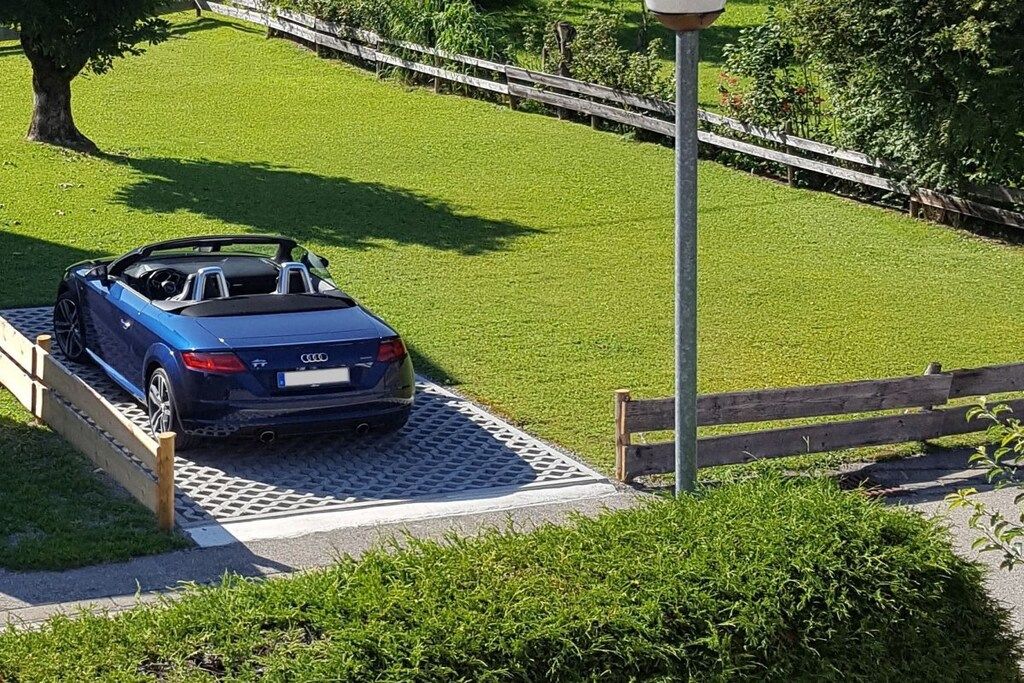 A blue convertible car parked on a grassy area with a wooden fence and a lamppost in the background.