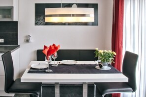 Mesa de jantar posta com pratos, talheres e um arranjo de flores vermelhas.