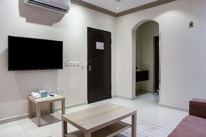 A hotel room with a flat-screen TV, a small table with a phone and tissues, a door with a sign, and a bathroom visible through an archway. - OYO 628 Wasan Suites (Riyadh)