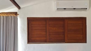 Una cama con cabecera de madera, dos mesitas de noche con lámparas y un equipo de aire acondicionado en la pared.