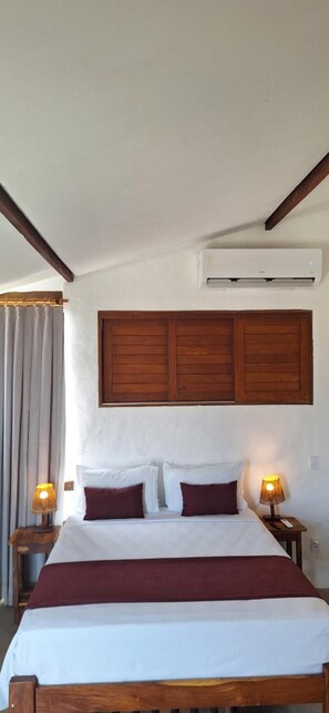 Uma cama com cabeceira de madeira, duas mesas de cabeceira com luminárias e um aparelho de ar condicionado na parede.