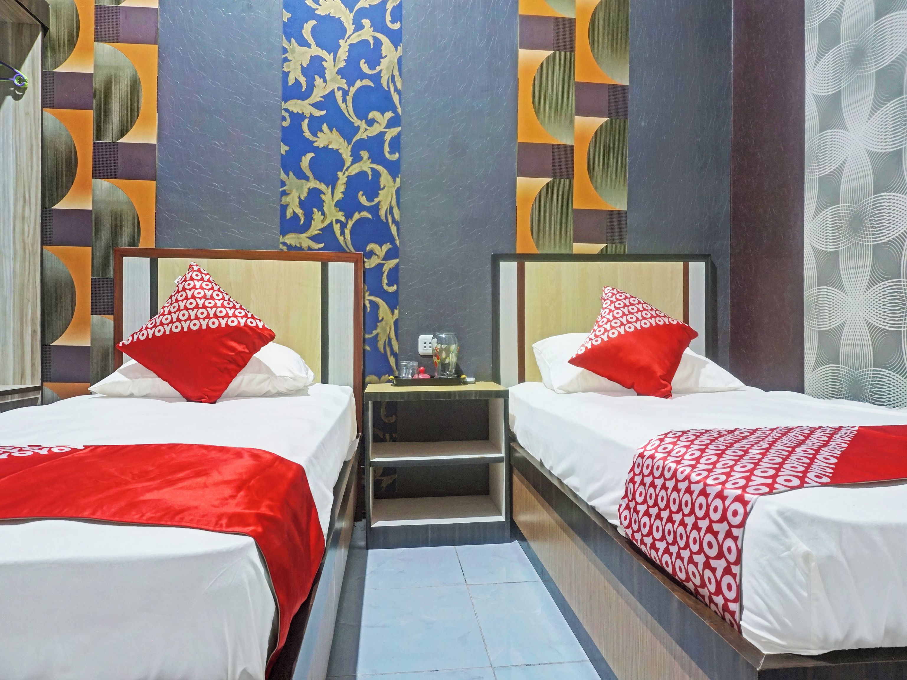 A hotel room with two beds, each with a red and white patterned bedspread, a nightstand with a lamp, and a mirror.