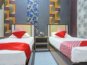 A hotel room with two beds, each with a red and white patterned bedspread and matching pillows. The room features a modern design with patterned wallpaper and a small bedside table with a lamp. - Collection O 91488 Hotel Lingkarsut Jeneponto (Jeneponto)