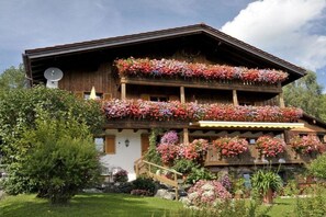 A chalet with multiple balconies adorned with flowers, a satellite dish, and a stone foundation. - Hefle in the Gottstein House (Bad Hindelang)