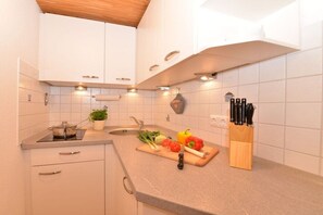 A kitchen with white cabinets, a countertop, a sink, a cutting board with vegetables, and a knife block. - Hefle in the Gottstein House (Bad Hindelang)