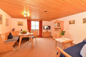 A cozy room with a wooden ceiling, a dining area with a table and chairs, a sofa, a television, and a cabinet. - Hefle in the Gottstein House (Bad Hindelang)