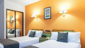 Ein Hotelzimmer mit zwei Betten, einem Nachttisch mit Telefon und einer Wandlampe.