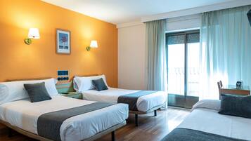 A hotel room with two beds, a window with curtains, and a wall-mounted lamp.