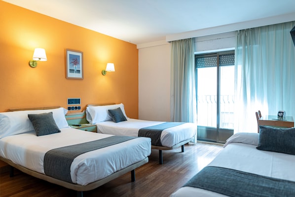 Une chambre d’hôtel avec deux lits, une fenêtre avec des rideaux et une lampe fixée au mur.
