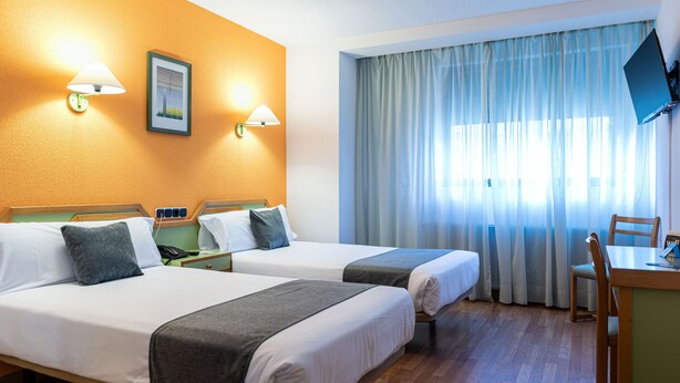 Ein Hotelzimmer mit zwei Betten, einem Schreibtisch, einem Stuhl und einem Fernseher an der Wand.