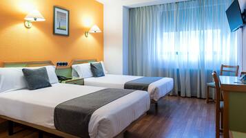 A hotel room with two beds, a desk, a chair, and a TV on the wall.