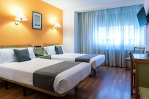 Une chambre d’hôtel avec deux lits, un bureau, une chaise et un téléviseur fixé au mur.