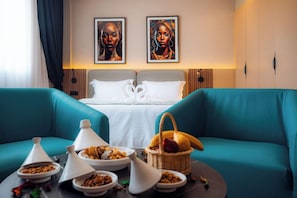 A hotel room with a bed, two blue sofas, a dining table with food, and two framed artworks on the wall. - Elite View Hotel Dakhla (Dakhla)