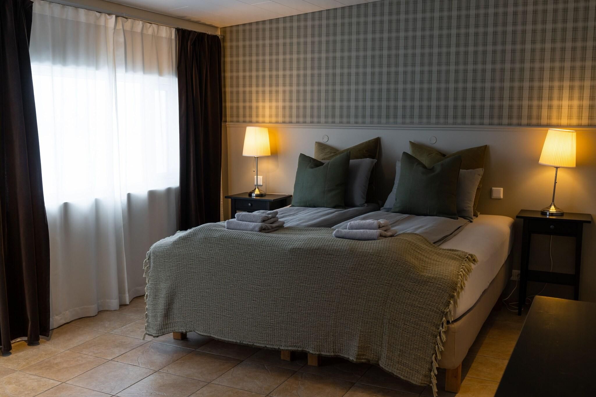 Ein Hotelzimmer mit einem Bett, zwei Nachttischen, einem fenster mit Vorhängen und einem Kopfteil mit Karomuster.