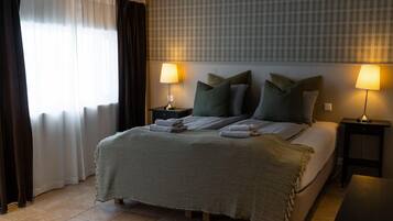 A hotel room with a bed, two bedside tables, a window with curtains, and a headboard with a plaid pattern.