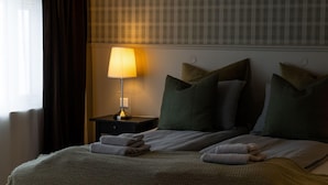 Ein Hotelzimmer mit Bett, Kissen, einem Nachttisch mit Lampe und einem Fenster mit Vorhängen.