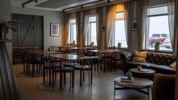 A spacious lounge area with multiple seating options, including tables and sofas, arranged around large windows offering a view of the outside.