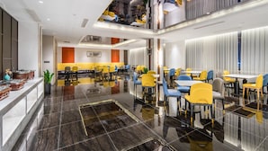 Uma área de jantar moderna com piso polido, várias mesas e cadeiras, e teto alto com luminárias pendentes.