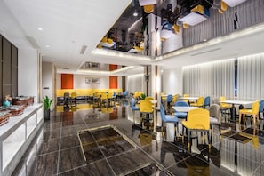 Una zona de dinar moderna amb un sòl polit, diverses taules i cadires, i un sostre alt amb llums penjants.