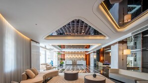 Um hall de hotel moderno com teto alto, área de estar central e balcão de recepção.