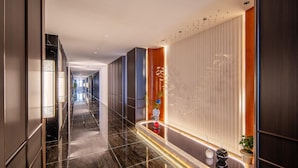 Corredor moderno de hotel com piso refletivo, balcão de recepção e planta na parede.