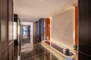 Passadís d'hotel modern amb un terra reflectant, una recepció i una planta penjant a la paret.