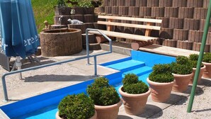 Un espace piscine avec des marches menant à l’eau, entouré de jardinières en terre cuite et d’un banc en bois.