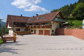Ein zweigeschossiges Gebäude mit einem geneigten Dach, einem Balkon mit Blumenkästen und einem gepflasterten Innenhof.