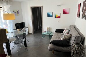 A modern living room with a glass dining table, a sofa, and a television. - Holiday apartment with 1 bedroom (COLMAR)