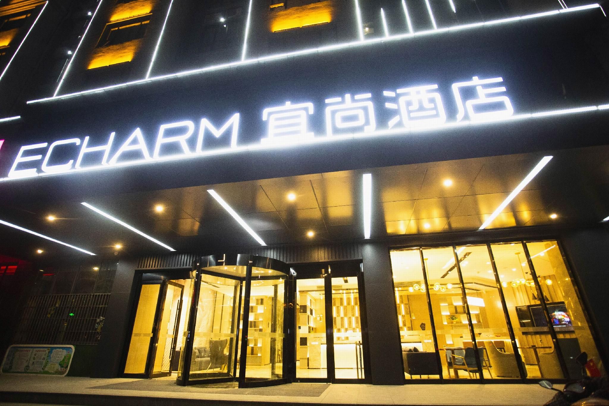 A hotel entrance with a modern design, featuring a prominent illuminated sign and a glass facade.