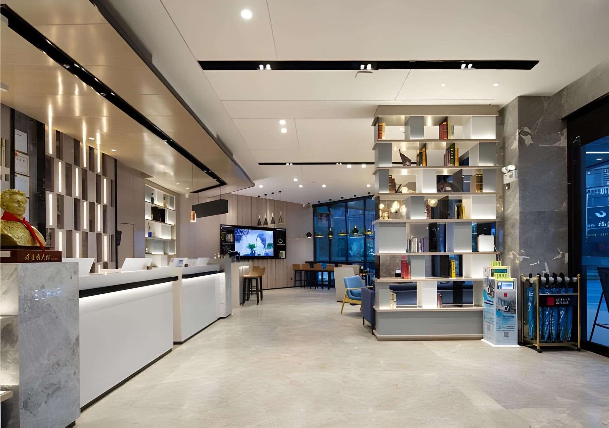 A modern hotel lobby with a reception desk, seating area, and a large bookshelf.