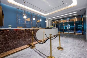 A hotel reception area with a marble counter, gold stanchions, and a modern ceiling design.