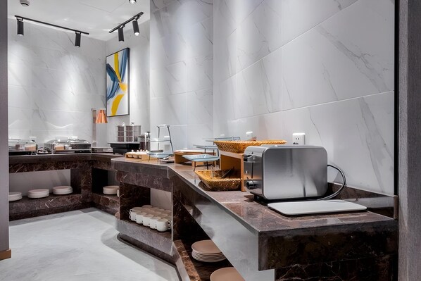 Une cuisine moderne avec des plans de travail en marbre, un coin café et un grand tableau abstrait accroché au mur.