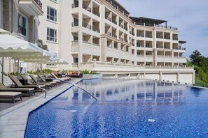 A hotel with a swimming pool, multiple balconies, and sun loungers.