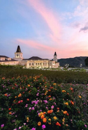 A large building with two towers, surrounded by a garden with colorful flowers. - Twin Lakes Hotel (Laurel)