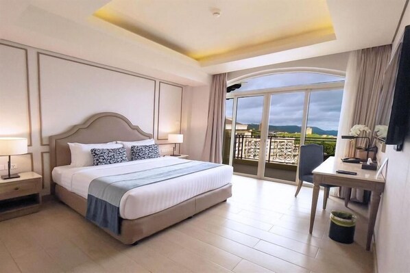 A hotel room with a large bed, a desk, and a balcony with a view.